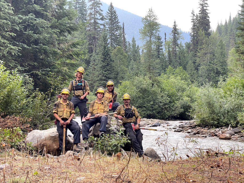 A team of wildfire fighters taking a break for a photo next to a running river.